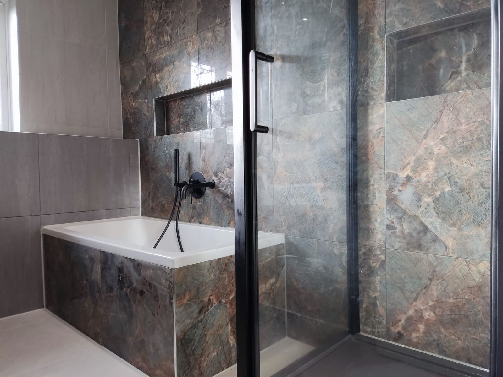 Dark marble bathroom with black framed shower screen and matt black taps in Hertfordshire