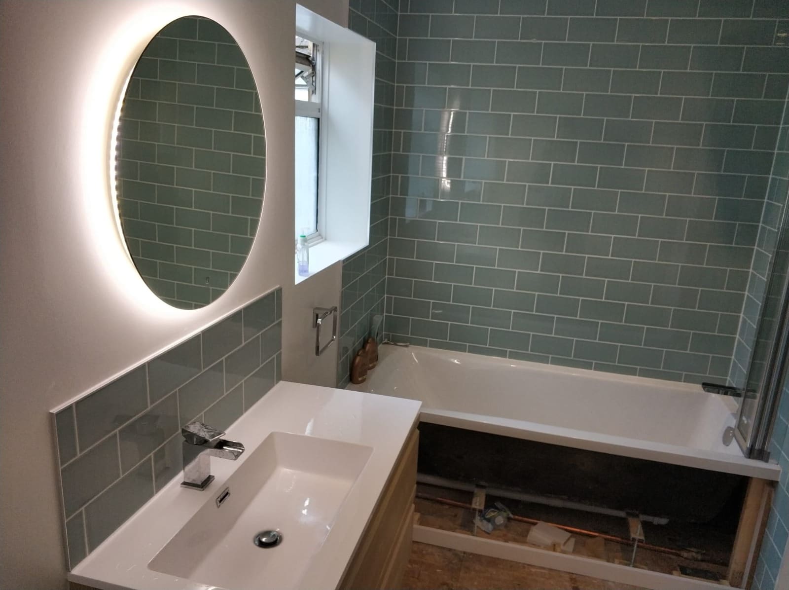 Green metro tiled bathroom with bath, LED mirror and vanity unit installation