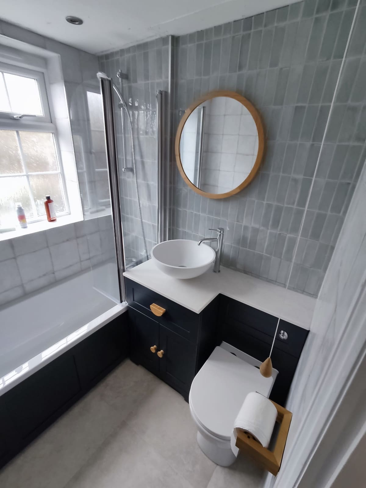 Sage green tiled family bathroom with navy vanity unit and round mirror